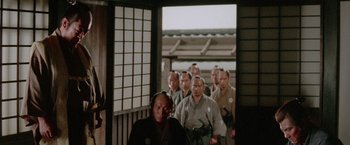 Movie still from “Lone Wolf and Cub: Baby Cart to Hades” (1972), directed by Kenji Misumi – A group of men standing next to each other in front of a building; Medium shot, Over the shoulder angle