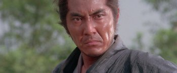 Movie still from “Lone Wolf and Cub: Baby Cart to Hades” (1972), directed by Kenji Misumi – An asian man with long brown hair wearing a black shirt; Close Up shot, Low angle
