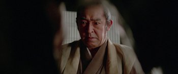 Movie still from “Lone Wolf and Cub: Baby Cart to Hades” (1972), directed by Kenji Misumi – An older man wearing a robe looking at the camera; Close Up shot, Over the shoulder angle