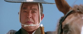 Movie still from “Lone Wolf and Cub: Baby Cart to Hades” (1972), directed by Kenji Misumi – An older asian man wearing a hat with a stick in his mouth; Close Up shot, Low angle