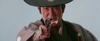 Movie still from “Lone Wolf and Cub: Baby Cart to Hades” (1972), directed by Kenji Misumi – A man with a hat is holding a toy gun; Close Up shot, Low angle