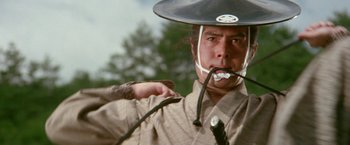 Movie still from “Lone Wolf and Cub: Baby Cart to Hades” (1972), directed by Kenji Misumi – A man wearing a cowboy hat with a whip in his mouth; Close Up shot, Low angle