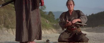 Movie still from “Lone Wolf and Cub: Baby Cart to Hades” (1972), directed by Kenji Misumi – A man holding a sword on the beach; Medium shot, High angle