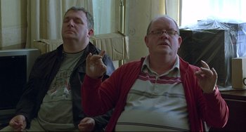 Movie still from “Looking for Eric” (2009), directed by Ken Loach – Two men sitting in a living room one of which is holding his finger up; Medium shot, Low angle