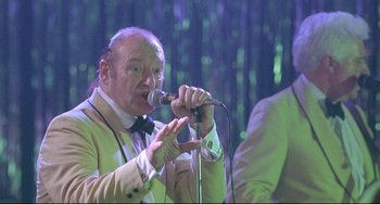 Movie still from “Looking for Eric” (2009), directed by Ken Loach – An older man in a white jacket is singing into a microphone; Close Up shot, Low angle