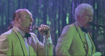 Movie still from “Looking for Eric” (2009), directed by Ken Loach – A man with a bow tie is singing into a microphone; Medium shot, Low angle
