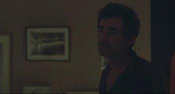 Movie still from “Looking for Eric” (2009), directed by Ken Loach – A man standing in a living room with his head turned to the side; Medium shot, Over the shoulder angle