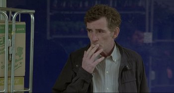 Movie still from “Looking for Eric” (2009), directed by Ken Loach – A man is smoking a cigarette while wearing a jacket; Medium shot, Over the shoulder angle