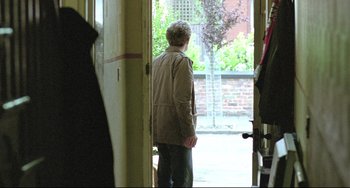 Movie still from “Looking for Eric” (2009), directed by Ken Loach – An older woman standing at the entrance of a house; Wide shot, Over the shoulder angle