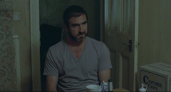Movie still from “Looking for Eric” (2009), directed by Ken Loach – A man sitting at a table with a cup in his hand; Medium shot, Over the shoulder angle