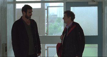 Movie still from “Looking for Eric” (2009), directed by Ken Loach – Two men standing next to each other in front of a window; Medium shot, Over the shoulder angle