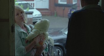 Movie still from “Looking for Eric” (2009), directed by Ken Loach – A woman holding a baby in her arms while standing next to a car; Medium shot, Over the shoulder angle
