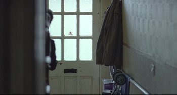 Movie still from “Looking for Eric” (2009), directed by Ken Loach – A coat hanging on a coat rack in front of an open door; Wide shot, Over the shoulder angle