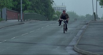 Movie still from “Looking for Eric” (2009), directed by Ken Loach – A man riding a bike down a street; Wide shot, High angle