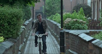 Movie still from “Looking for Eric” (2009), directed by Ken Loach – A man riding a bike down a brick walkway; Wide shot, Low angle