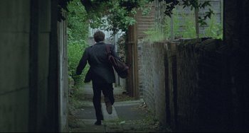 Movie still from “Looking for Eric” (2009), directed by Ken Loach – A man walking down a street holding a bag; Wide shot, High angle