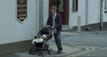 Movie still from “Looking for Eric” (2009), directed by Ken Loach – A man pushing a baby in a stroller down a street; Wide shot, Low angle