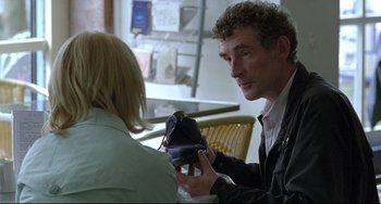 Movie still from “Looking for Eric” (2009), directed by Ken Loach – A man holding a shoe in his hand while talking to a woman; Close Up shot, Over the shoulder angle