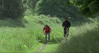 Movie still from “Looking for Eric” (2009), directed by Ken Loach – Two men are walking through a lush green field; Wide shot, Low angle