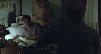 Movie still from “Looking for Eric” (2009), directed by Ken Loach – A man sitting on the floor reading a book; Medium shot, Over the shoulder angle
