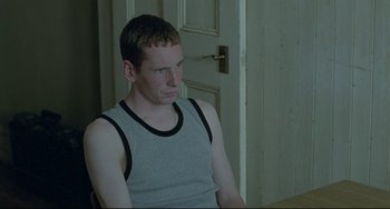 Movie still from “Looking for Eric” (2009), directed by Ken Loach – A man sitting in front of a white door; Medium shot, Over the shoulder angle