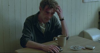 Movie still from “Looking for Eric” (2009), directed by Ken Loach – A man sitting at a wooden table with a cup of coffee; Medium shot, High angle