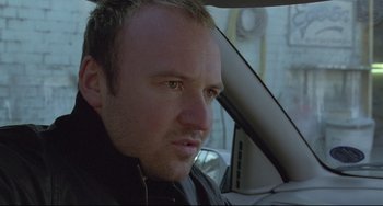 Movie still from “Looking for Eric” (2009), directed by Ken Loach – A person sitting in a car looking at the camera; Close Up shot, High angle