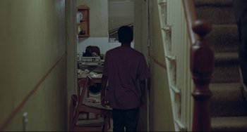 Movie still from “Looking for Eric” (2009), directed by Ken Loach – A man walking through a hallway towards a table; Wide shot, High angle