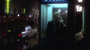 A man talking on a phone in a phone booth at night