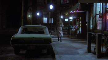 A woman is walking down the street by a vintage car
