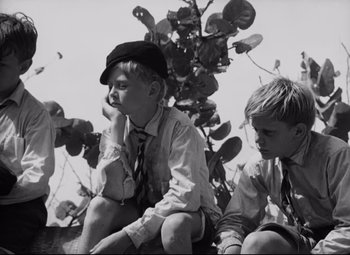 Movie still from “Lord of the Flies” (1963), directed by Peter Brook – Two young boys sitting next to each other on the ground; Medium shot, Low angle