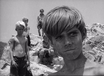 Movie still from “Lord of the Flies” (1963), directed by Peter Brook – A black and white photo of a young boy and some other young men; Close Up shot, Low angle