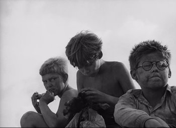 Movie still from “Lord of the Flies” (1963), directed by Peter Brook – A group of young men sitting next to each other on the ground; Medium shot, High angle