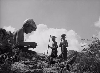 Movie still from “Lord of the Flies” (1963), directed by Peter Brook – A black - and - white photo of three people on a rocky hill; Wide shot, Low angle