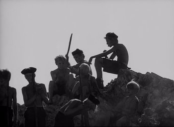 Movie still from “Lord of the Flies” (1963), directed by Peter Brook – A black and white photo of a group of people sitting on a rock; Wide shot, High angle