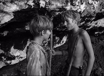 Movie still from “Lord of the Flies” (1963), directed by Peter Brook – Two young boys are standing in a cave; Medium shot, High angle