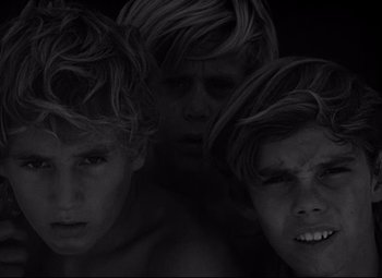 Movie still from “Lord of the Flies” (1963), directed by Peter Brook – Three young men with long blonde hair and one with blond hair and one with brown hair; Close Up shot, High angle