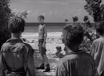 Movie still from “Lord of the Flies” (1963), directed by Peter Brook – A group of young men standing on top of a sandy beach; Wide shot, Over the shoulder angle