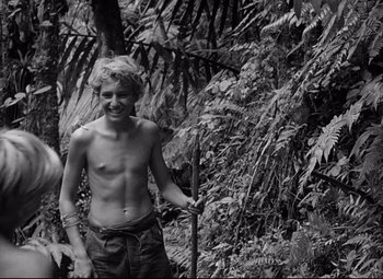Movie still from “Lord of the Flies” (1963), directed by Peter Brook – A young man holding a stick in the woods; Medium shot, High angle
