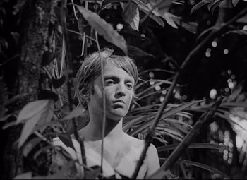Movie still from “Lord of the Flies” (1963), directed by Peter Brook – A young man standing in the middle of a forest; Medium shot, Low angle