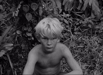 Movie still from “Lord of the Flies” (1963), directed by Peter Brook – A young boy sitting in the grass near a tree; Close Up shot, High angle