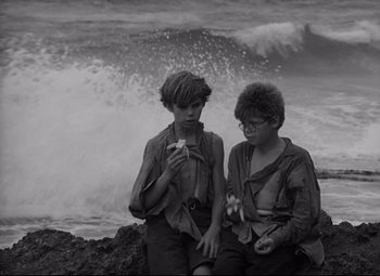 Movie still from “Lord of the Flies” (1963), directed by Peter Brook – Two young men sitting on a rock near the ocean; Medium shot, High angle