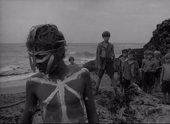 Movie still from “Lord of the Flies” (1963), directed by Peter Brook – A black and white photo of a group of people standing on a beach; Wide shot, High angle