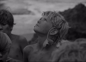 Movie still from “Lord of the Flies” (1963), directed by Peter Brook – A young man listening to music while standing next to a body of water; Close Up shot, Low angle