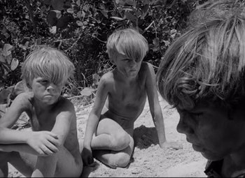 Movie still from “Lord of the Flies” (1963), directed by Peter Brook – A group of children sitting in the sand on a beach; Medium shot, High angle