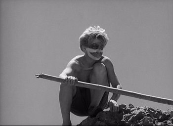Movie still from “Lord of the Flies” (1963), directed by Peter Brook – A young man holding onto a stick while crouching on top of a mountain; Close Up shot, Low angle