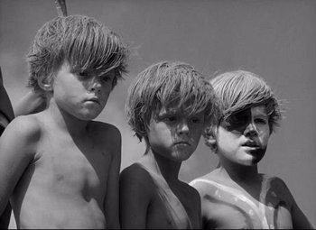 Movie still from “Lord of the Flies” (1963), directed by Peter Brook – A group of three young boys standing next to each other; Close Up shot, Low angle