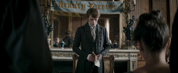 Movie still from “Lost Illusions” (2021), directed by Xavier Giannoli – A man in a suit and tie holding a piece of paper in his hands; Medium shot, Over the shoulder angle