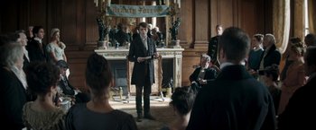 Movie still from “Lost Illusions” (2021), directed by Xavier Giannoli – A man standing in front of a group of people in a room; Medium shot, Over the shoulder angle