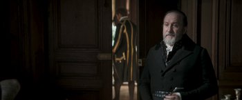 Movie still from “Lost Illusions” (2021), directed by Xavier Giannoli – A man standing in front of a door wearing a suit and tie; Medium shot, Over the shoulder angle
